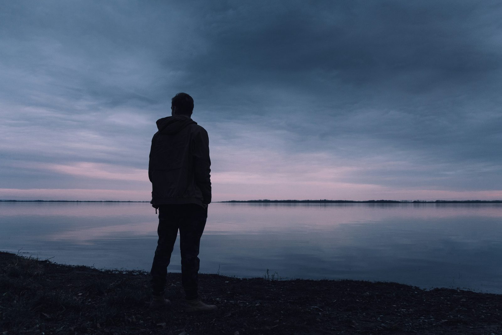 A man standing alone in muted light, representing male loneliness, men's therapy in Ontario